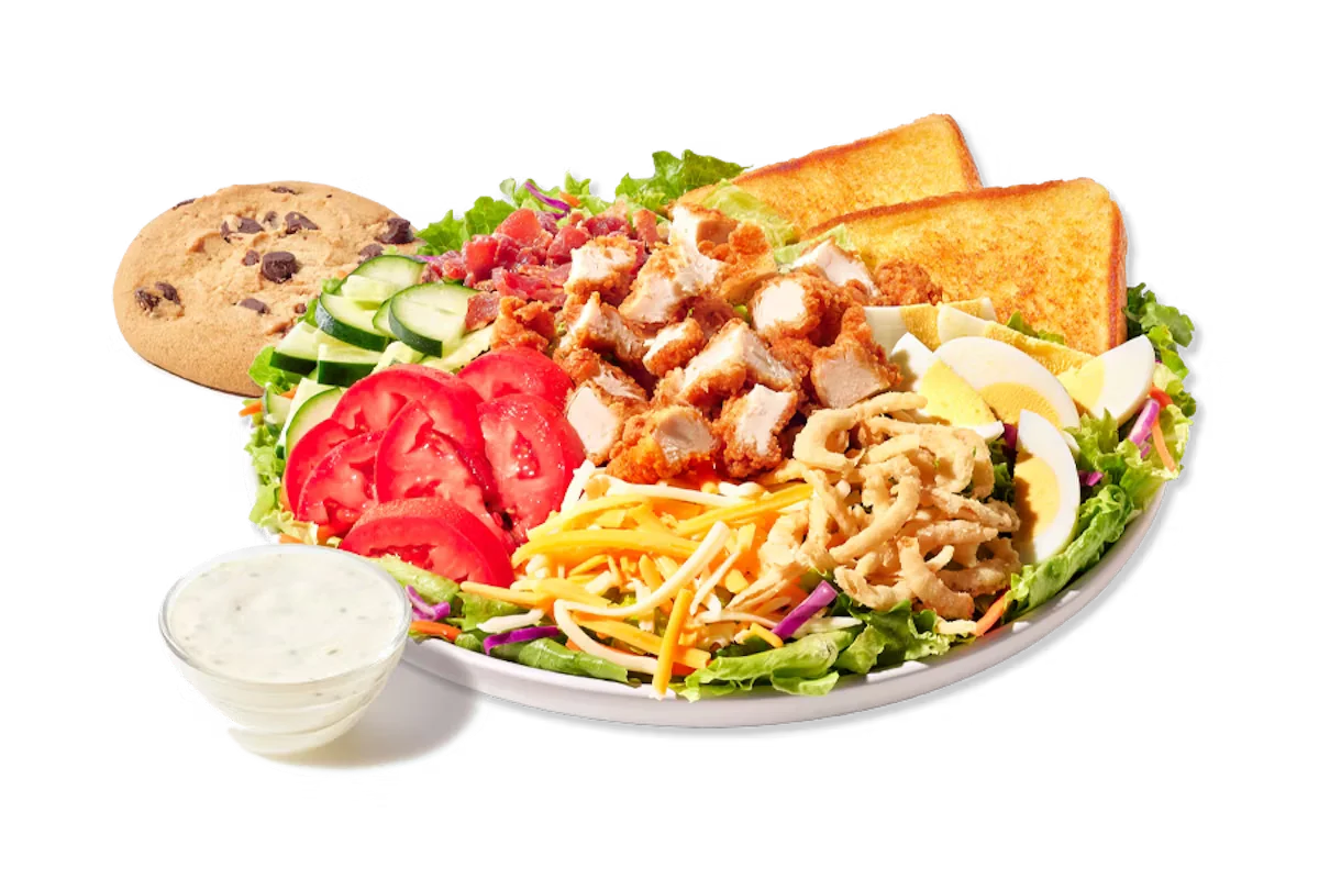 Zaxby's Cobb Zalad® Boxed Lunch, featuring a fresh salad with grilled or fried chicken, bacon, hard-boiled egg, Cheddar Jack cheese, cucumbers, tomatoes, and fried onions, accompanied by Texas Toast and a chocolate chip cookie.