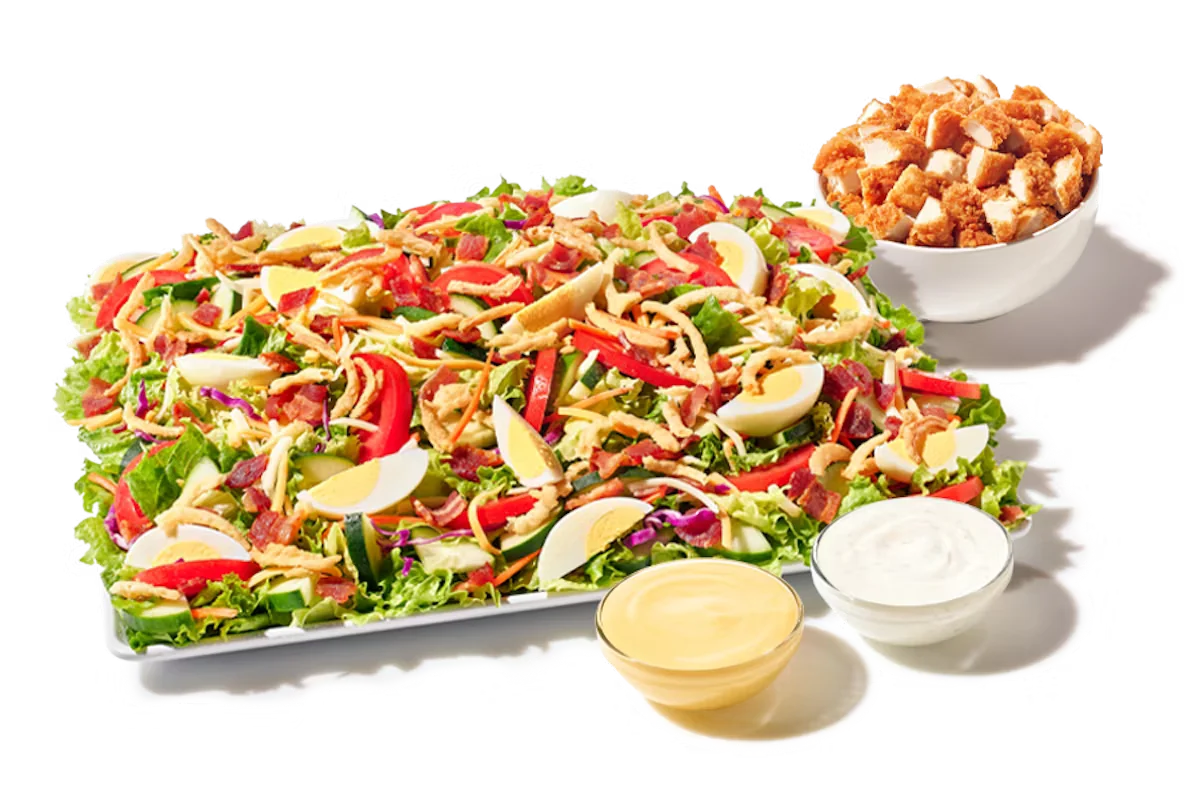 Zaxby’s Cobb Zalad® Platter featuring crispy Chicken Fingerz™, hard-boiled egg, bacon, mixed greens, cucumbers, tomatoes, shredded cheese, and fried onions.