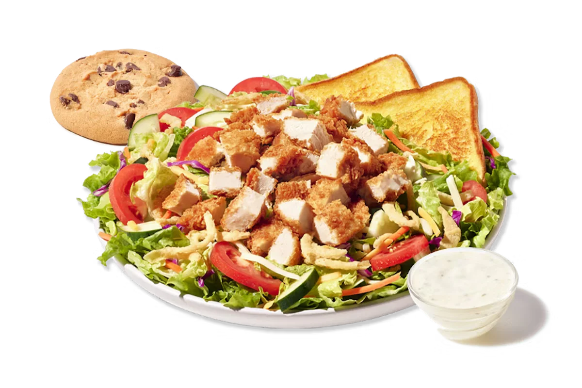 Zaxby's House Zalad Boxed Lunch, featuring a bed of mixed greens with carrots and red cabbage, topped with Cheddar Jack cheese, cucumbers, tomatoes, and fried onions, accompanied by fried or grilled chicken, Texas Toast, and a chocolate chip cookie.